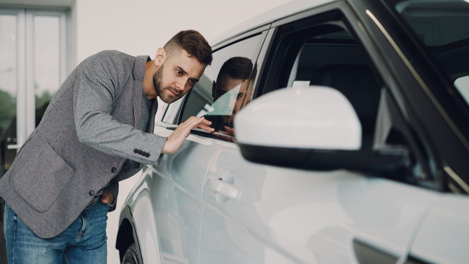 Man carefully examining a modern white car at a dealership showroom.